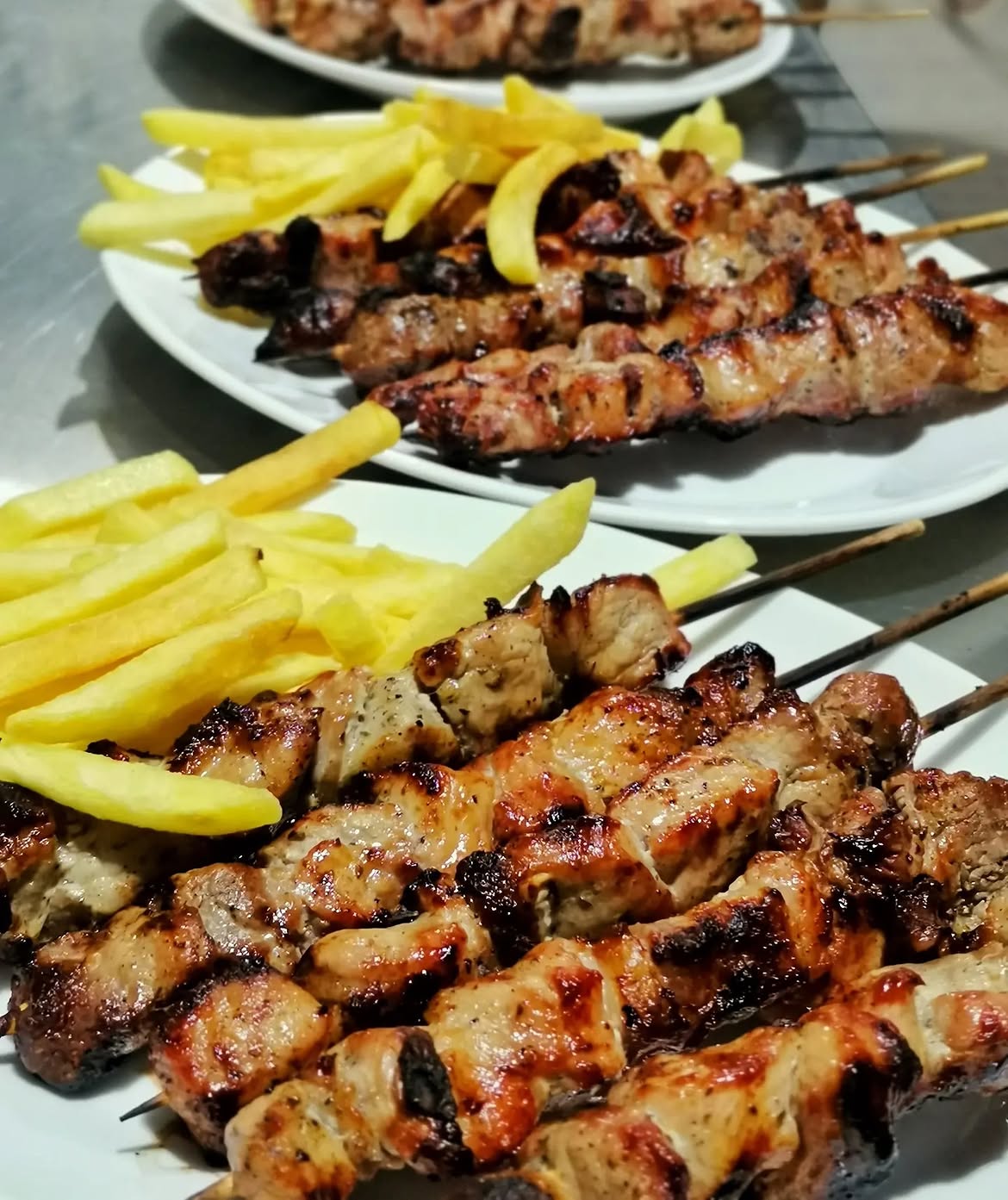 Ψητά χοιρινά σουβλάκια με τηγανητές πατάτες σε λευκά πιάτα, έτοιμα για σερβίρισμα