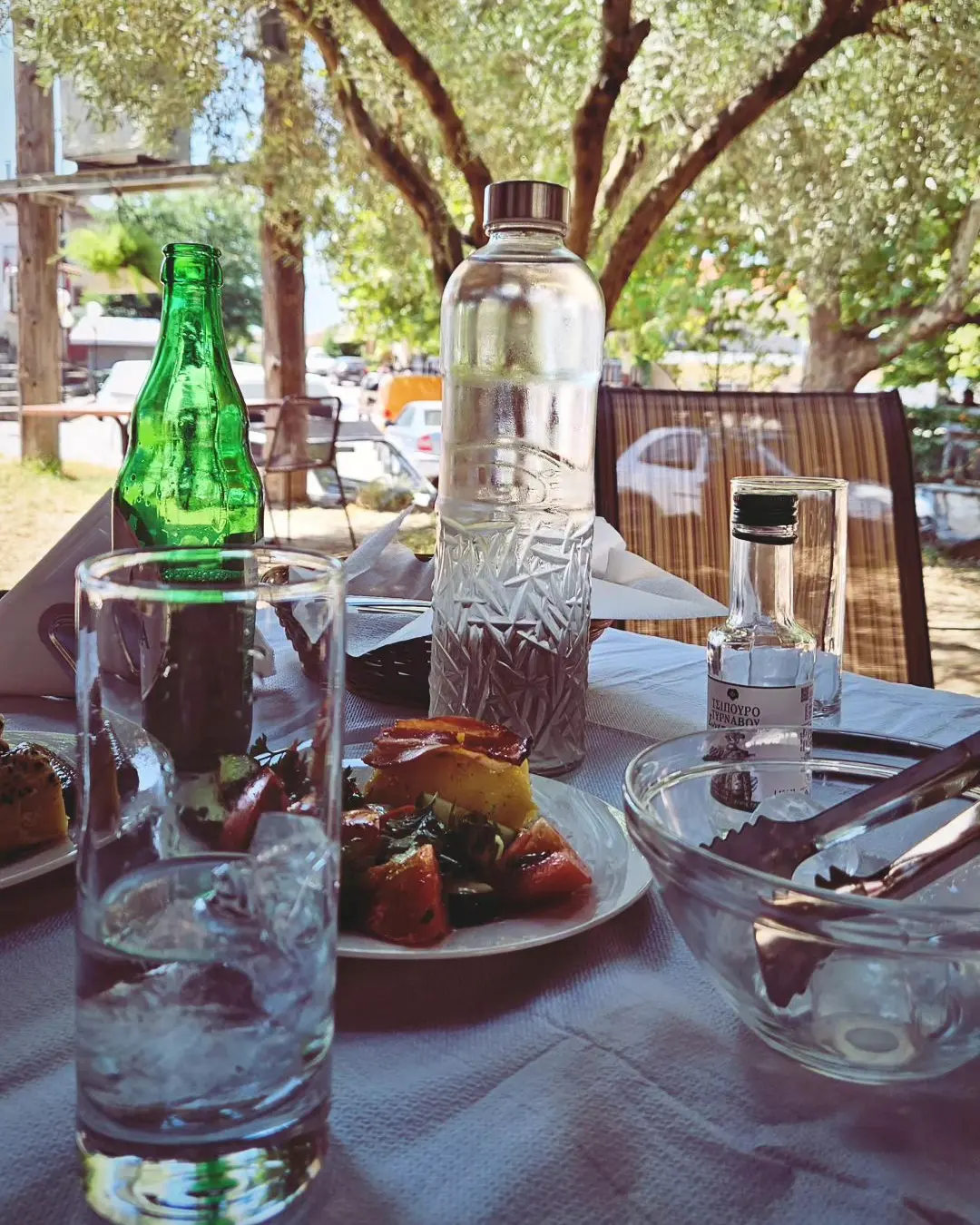 Τραπέζι στην αυλή κάτω από ελιές, με τσίπουρο, νερό και σαλάτα για την κυριακάτικη τσιπουροκατάσταση